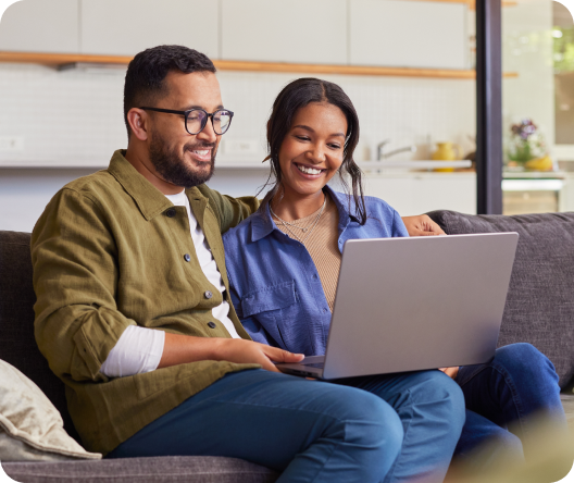 Smiling couple sitting on a couch using a laptop together at home